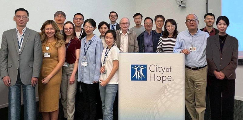 Group photo of 17 Binghui Shen lab members around a City of Hope podium